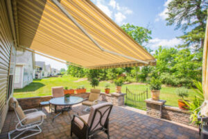 A tan awning extends over a paver patio with a table and chairs
