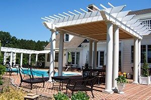 A white pergola with a retractable cover sits near a pool