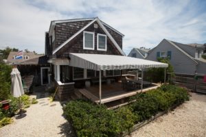 Large striped awning covers patio on two-story beach home