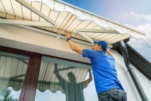 Worker installs retractable awning over house window