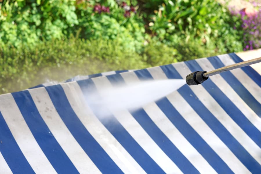 Power washer spraying water on white and blue awning